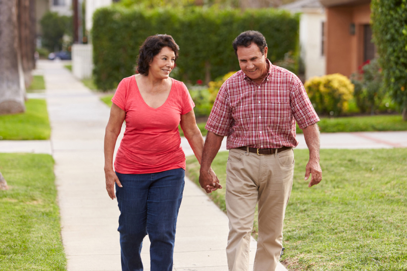 Senior Hispanic couple walking and holding hands on a sidewalk.