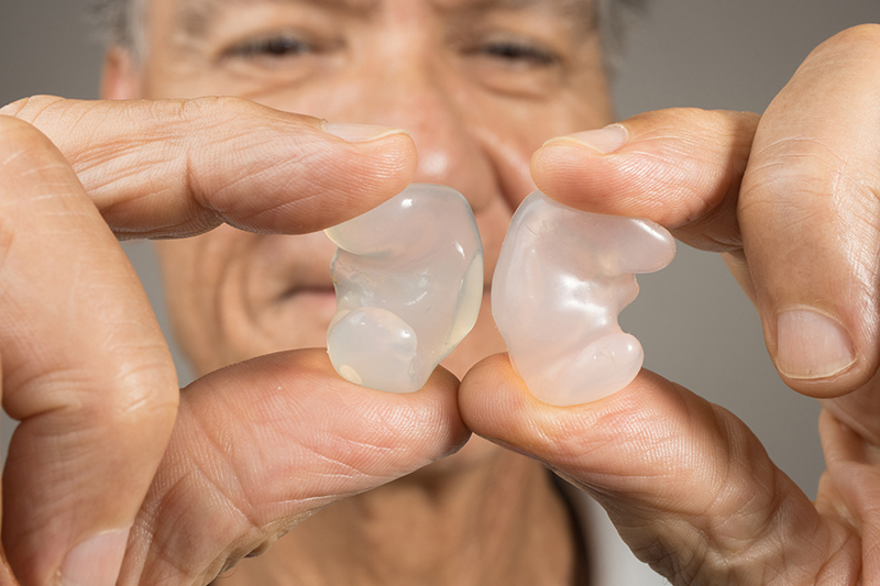 Older man holding up clear earplugs between two fingers.