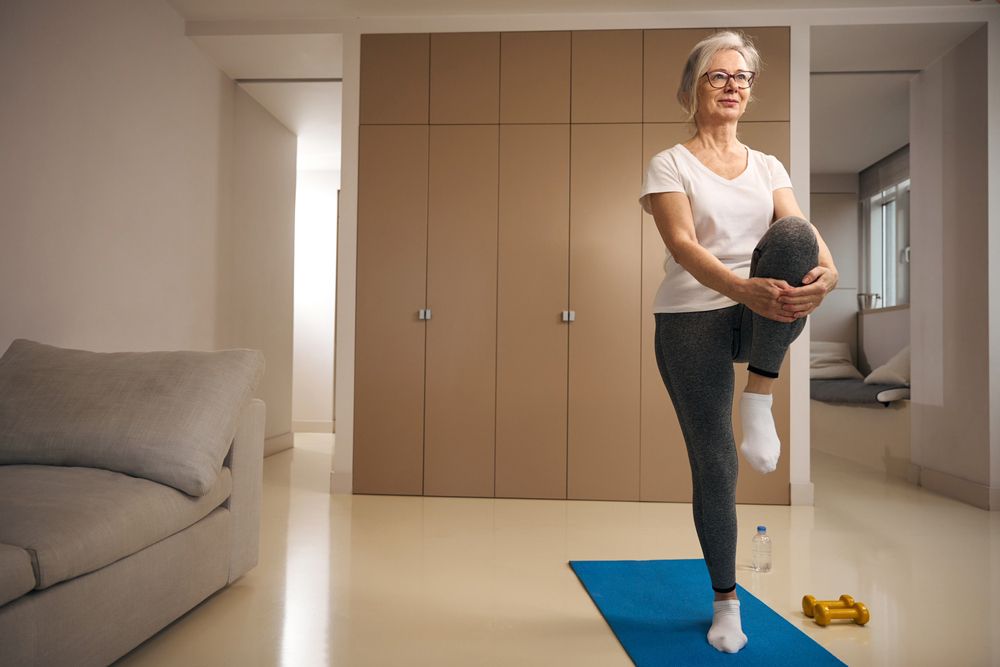 Older woman standing on one leg on a yoga mat while holding other leg.