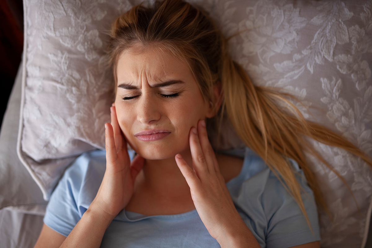 Girl holding her jaw and clenching her teeth while laying down.