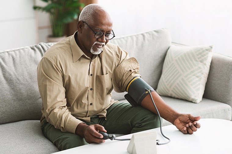 Older adult man taking his blood pressure at home while sitting on a couch.