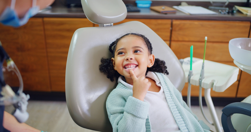 Child pointing to their teeth while sitting in a dental office chair.