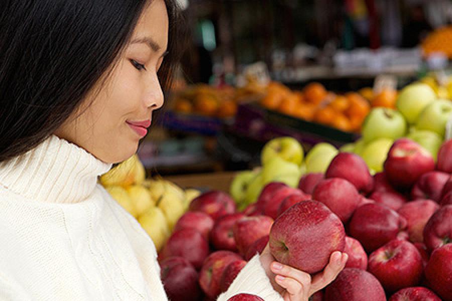 Young woman in grocery store looking at apples.