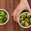 Person's hand choosing brussel sprouts over broccoli Person's hand choosing brussel sprouts over broccoli
