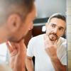 Man looking in the mirror at the gray hair in his beard Man looking in the mirror at the gray hair in his beard