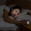 Woman awake in bed touching the alarm clock Woman awake in bed touching the alarm clock