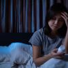 Woman sitting up in bed reading a pill bottle Woman sitting up in bed reading a pill bottle