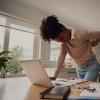 Young woman standing and holding her back while working on a laptop at home Young woman standing and holding her back while working on a laptop at home