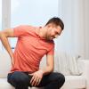 Man sitting on couch holding lower back while wincing in pain Man sitting on couch holding lower back while wincing in pain.
