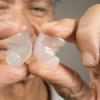 Older man holding up clear earplugs between two fingers.