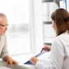 Doctor pointing out something on clipboard to older adult man.
