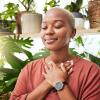 Young black woman meditating among plants indoors.