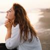 Woman with her eyes closed and hands clasped sitting next to the sea.