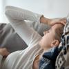 Woman laying on a couch with her hand on her head.