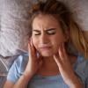 Girl holding her jaw and clenching her teeth while laying down.