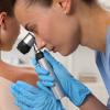 Health care provider looking at moles on the shoulder of a female patient using a dermatoscope.