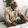 Older adult man taking his blood pressure at home while sitting on a couch.