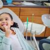 Child pointing to their teeth while sitting in a dental office chair.