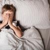 Child covering face while laying in bed with their stuffed animal.