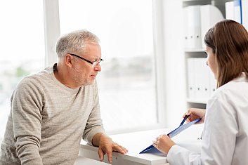 Doctor pointing out something on clipboard to older adult man.