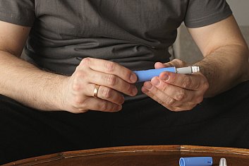 Man sitting on a couch preparing a GLP-1RA injection.
