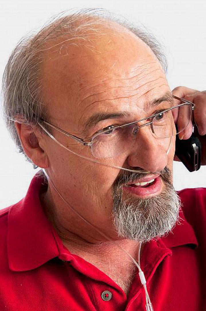 Man talking on phone while breathing in oxygen through a thin nasal tube.