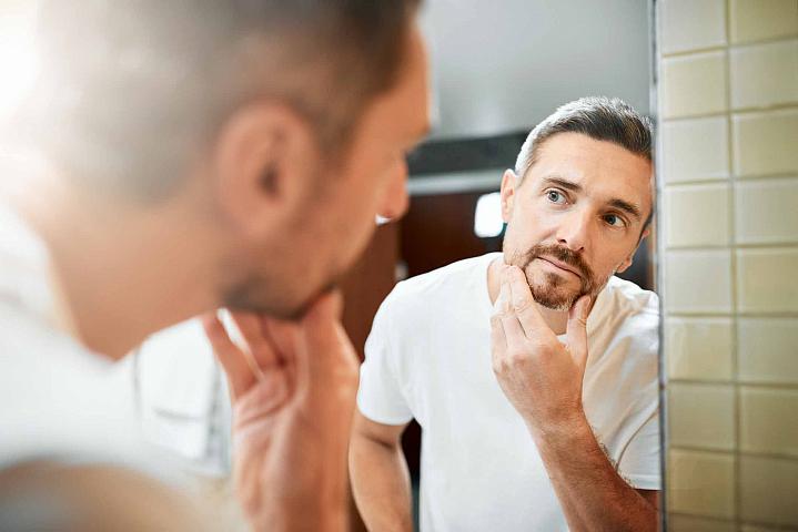 Man looking in the mirror at the grey hair in his beard
