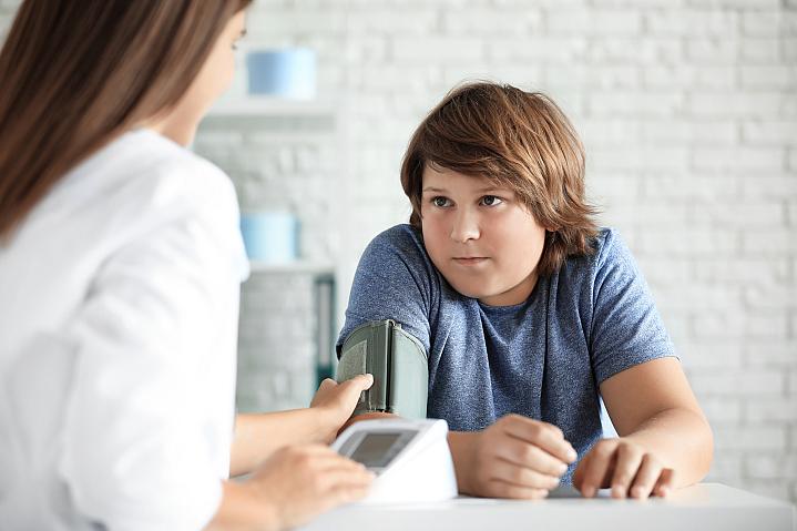 Boy who is overweight getting his blood pressure checked by health care professional.
