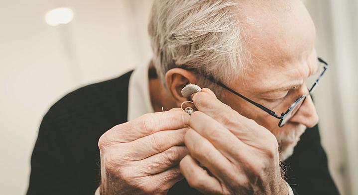 Older man placing a hearing aid in his ear.